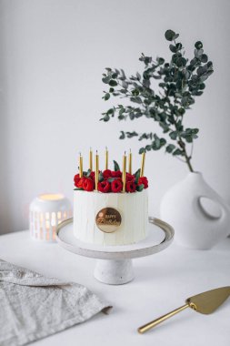 Beyaz arka planda mumları ve çiçekleri olan düğün pastası