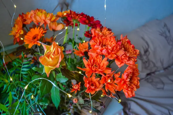 Bir buket çiçek, ateş gibi kırmızı ve bir ışık dekoru. Bir bukette çiçekler: Germini, Gerbera, Rose.