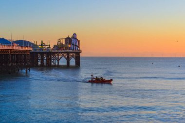 Gün batımı ve bir cankurtaran botu Brighton 'daki büyük rıhtımın altında yelken açıyor.
