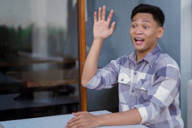 Bir adam kafede oturuyor, çok mutlu görünüyor, elini sallıyor sanki uzaktaki birine sesleniyormuş gibi.