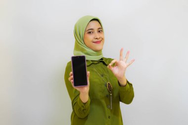 Mutlu Asyalı kadın reklam konsepti için telefonunu tutuyor. Yeşil kıyafet tesettür kadın konsepti