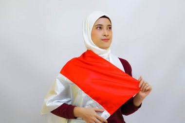 Indonesian muslim woman wearing hijab with proud gesture while holding Indonesia's flag. Indonesia's independence day concept clipart