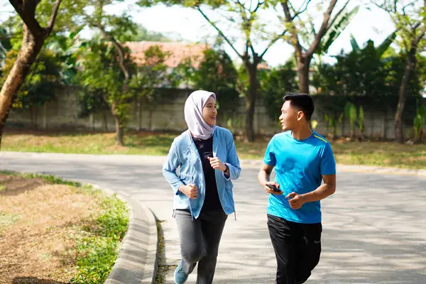 Young muslim couple happy together running at green summer park. Man and woman in hijab doing morning workout outdoors.
