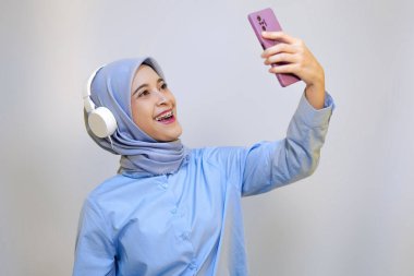 Genç Asyalı kadın kulaklıkla müzik dinlerken selfie çekiyor. Selfie ve müzik konsepti