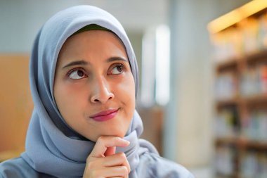 Zeki genç Müslüman kadın kütüphanede bir şey düşünürken yukarı bakıyor. eğitim ve kütüphane kavramı