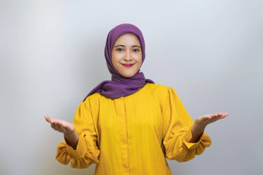 Beyaz stüdyo arka planında izole edilmiş avuç içinin fotokopisini gösteren tesettür ve sarı elbise giyen güzel Asyalı kadın portresi.