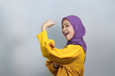 Yan yana genç Asyalı Müslüman kadın sarı kıyafet ve tesettüre bürünmüş kol kasları beyaz arka planda izole edilmiş gücü gösteriyor.. 