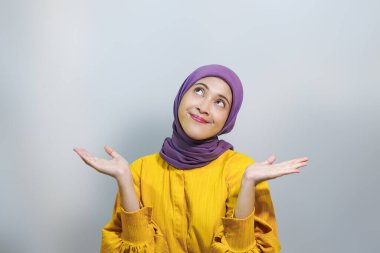 Beyaz stüdyo arka planında izole edilmiş avuç içinin fotokopisini gösteren tesettür ve sarı elbise giyen güzel Asyalı kadın portresi.