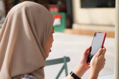 Hijab 'da telefon kullanan kadın. Plaj salonunda cep telefonuyla meşgul olan tesettürlü bir kadının tasviri..