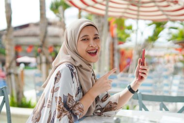 Hijab 'da telefon kullanan kadın. Plaj salonunda cep telefonuyla meşgul olan tesettürlü bir kadının tasviri..