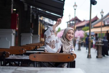 Endonezyalı Hijabi Kadını Uzaktan El sallıyor ya da Kafe görevlisini arıyor ya da Arkadaşını Arıyor