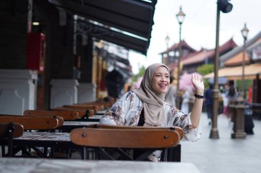 Endonezyalı Hijabi Kadını Uzaktan El sallıyor ya da Kafe görevlisini arıyor ya da Arkadaşını Arıyor