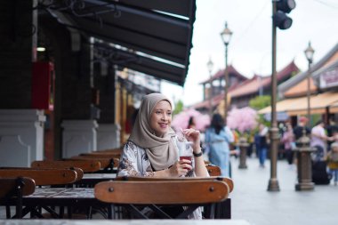 Endonezyalı Hijabi Kadını Cafe Bench 'te gülümsüyor. Kafe konseptinde neşeli anlar.
