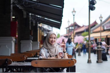 Endonezyalı Hijabi Kadını Cafe Bench 'te gülümsüyor. Kafe konseptinde neşeli anlar.