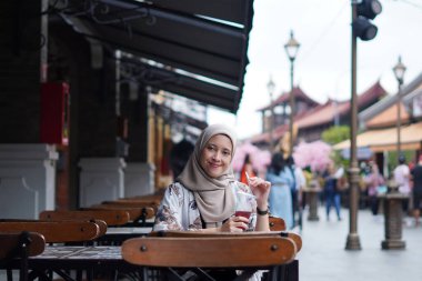 Endonezyalı Hijabi Kadını Cafe Bench 'te gülümsüyor. Kafe konseptinde neşeli anlar.