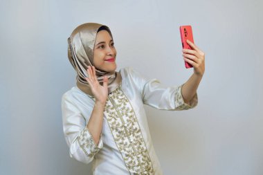 Endonezyalı Müslüman kadın akıllı telefon tutuyor, kamerayı doğrultuyor ve Ramazan ya da bayram kutlamalarında video için poz veriyor.