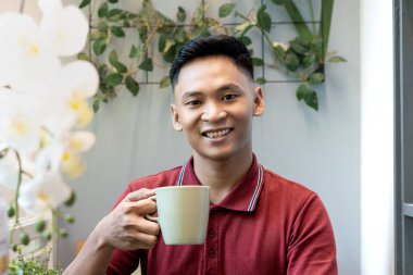 Balkonda oturan bir adam elinde yeşil ordu camlarıyla sağa, yakından bakıyor, hayal kuruyor ya da gülümserken düşünüyor, düşüncelere dalıyor.