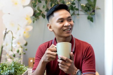 Balkonda oturan bir adam elinde yeşil ordu camlarıyla sağa, yakından bakıyor, hayal kuruyor ya da gülümserken düşünüyor, düşüncelere dalıyor.