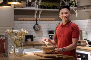 Yakışıklı ve mutlu genç adam yemek hazırlıyor, mutfaktaki ahşap kasede malzemeleri karıştırıyor.