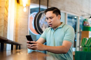 Yetişkin bir adam telefonundaki bir şeyden dolayı kızgın ve şok olmuş.