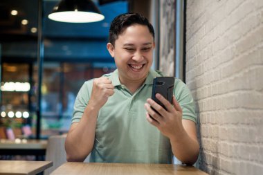 Modern bir kafede Asyalı bir adam Smartphone ile takılıyor. Telefon konseptiyle ilgili iyi haberler arıyor.