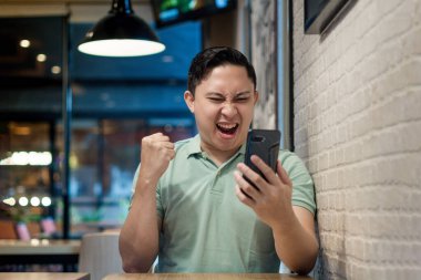 Modern bir kafede Asyalı bir adam Smartphone ile takılıyor. Telefon konseptiyle ilgili iyi haberler arıyor.