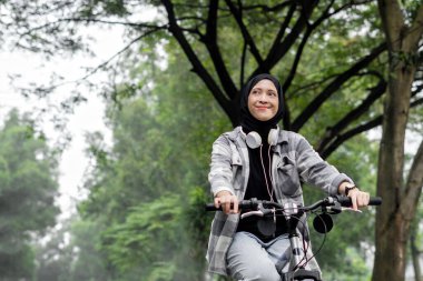 Genç, tesettürlü, rahat bir fanila giyen, bisiklet süren, dışarıda olmanın keyfini çıkaran neşeli bir kadın, kenara bak. İnsanlar aktif kentsel sağlıklı yaşam tarzı bisiklet konsepti.