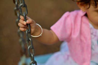 Salıncakta sallanıyor. Zincir salıncağı tutan küçük el. Küçük Hintli kız. Kız için pembe elbise. Salıncaktaki bebek