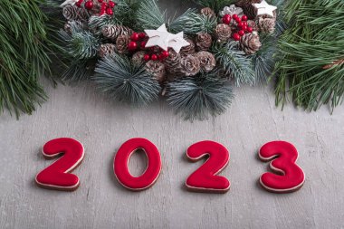 Kırmızı 2023 numara zencefilli çörek ve Noel çelengi. İyi yeni yıl ruhu. Arkaplanda açık gri duvar.