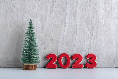 Küçük yapay bir Noel ağacı ve gri bir duvara karşı 2023 numaralı kırmızı numaralar. Yeni yıl konsepti. Boşluğu kopyala.