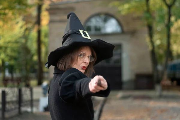 肖像画の女の子は黒の尖った帽子 コート 魔法の杖を身に着けています 眼鏡をかけた服の女 魔女の仕業だ — ストック写真