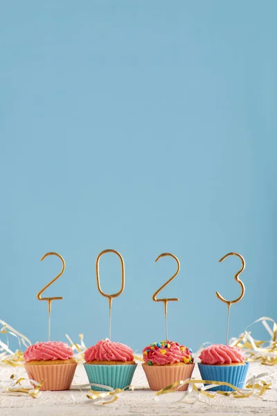 Happy New Year theme. Holiday muffins with pink butter cream and 2023 numbers on blue background. Vertical frame