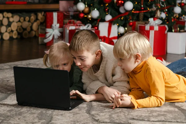 Drie Kinderen Liggen Grond Staren Naar Laptop Kerstboom Geschenken Achtergrond — Stockfoto