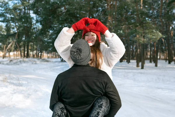 快乐的微笑的女孩保持着双手的心形 冬林背景下的年轻夫妇 阳光灿烂寒冷的日子 — 图库照片