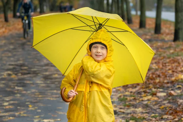 Portrait of smiling boy in yellow raincoat with large yellow umbrella in the autumn park. Happy child.
