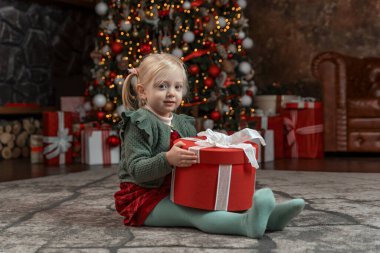 Şirin küçük sarışın kız büyük hediye kutusuyla süslü Noel salonunda oturuyor. Noel tatili. Yeni Yıl Dekorasyonu