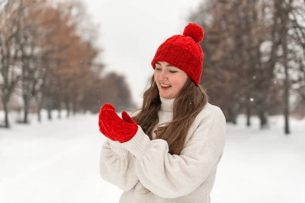 赤いニットの帽子をかぶった幸せな笑顔の若い女性と冬の公園の路地にミトン ポートレートの美しいです女の子でウールセーター — ストック写真