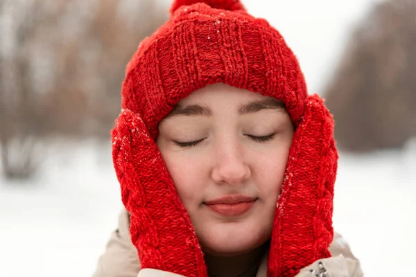 Fashionable red knitted hat and mittens on beautiful girl. Close-up face of woman in knitted headdress in outside.