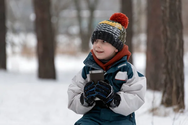 뜨거운 음료와 뜨거운 음료를 모자를 남자아이 눈덮인 공원에 — 스톡 사진