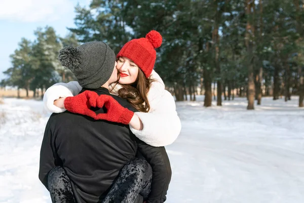 快乐的年轻女子手紧握着心形标志 拥抱她的男朋友 在冬季森林里的年轻夫妇 阳光灿烂 — 图库照片