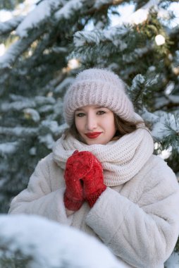 Güzel esmer, kırmızı eldivenli, beyaz şapkalı, karla kaplı köknar ağaçları arka planda bir kadın.