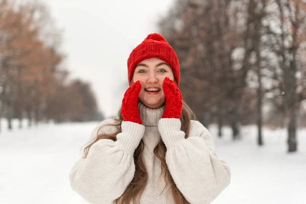 赤いニット帽とミトンとウールセーターの笑いの女の子の肖像 冬の公園で路地に — ストック写真