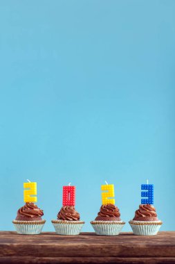 Mutlu yıllar 2023 teması. Ev yapımı çikolatalı kekler ve ahşap masada 2023 numaralı renkli mum. Dikey çerçeve, mavi arkaplan