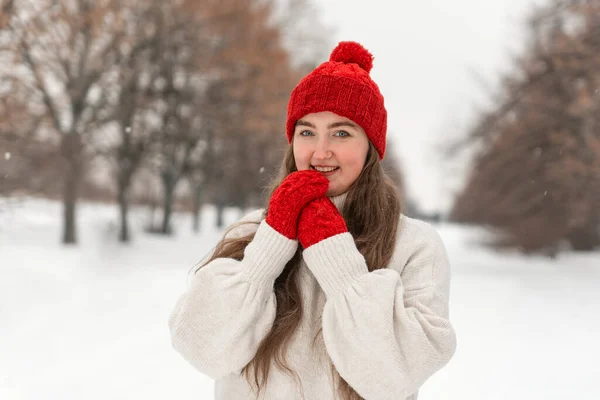 美しい若い女の子のカメラにまっすぐに ウールの赤い帽子とミトン笑顔 冬の公園でニットの服の女性 — ストック写真