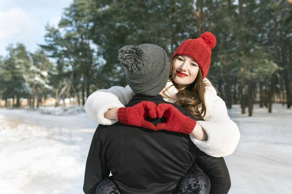 一对年轻夫妇在冬天的森林背景下 女孩手握着心形的标志 冬季晴天 — 图库照片