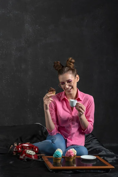 Смеющаяся Девушка Прической Булочки Очках Пьет Кофе Кексами Разноцветным Кремом — стоковое фото