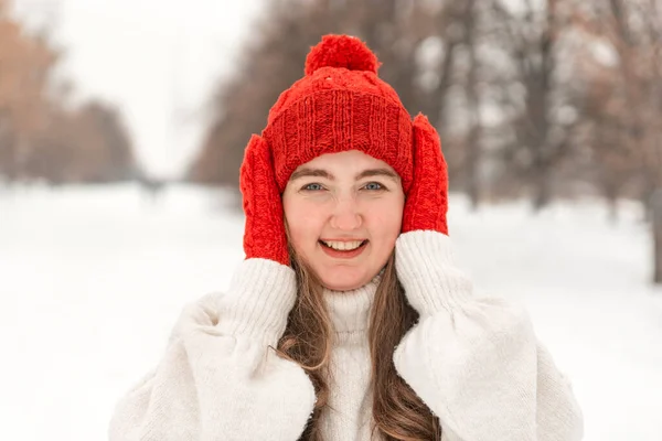 ニットの赤い帽子とミトンで美しい若い女性を笑っての肖像画 冬の公園を歩く女 — ストック写真