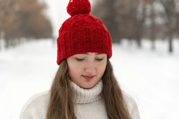 Modest young woman in red knitted hat in winter park. Portrait of woman in knitted headdress in outside.