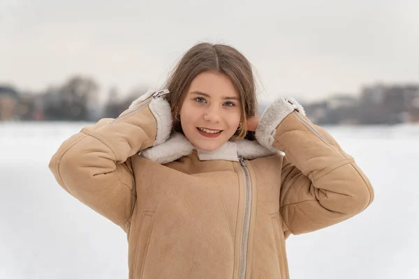 물결치는 베이지 코트를 미소짓는 소녀의 모습은 눈덮인 지형에서 머리카락을 — 스톡 사진
