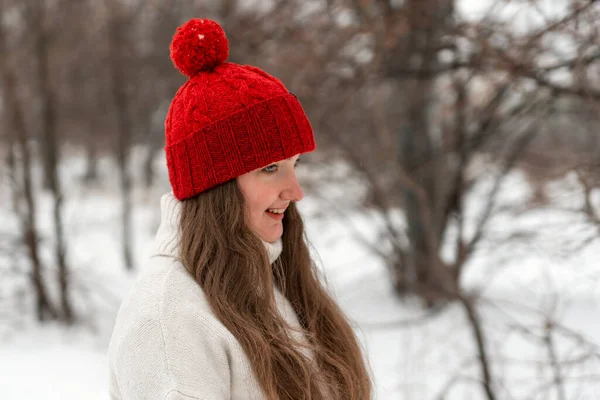 Smiling modest young woman in red knitted hat in winter park. Woman walk in knitted headdress in outside.